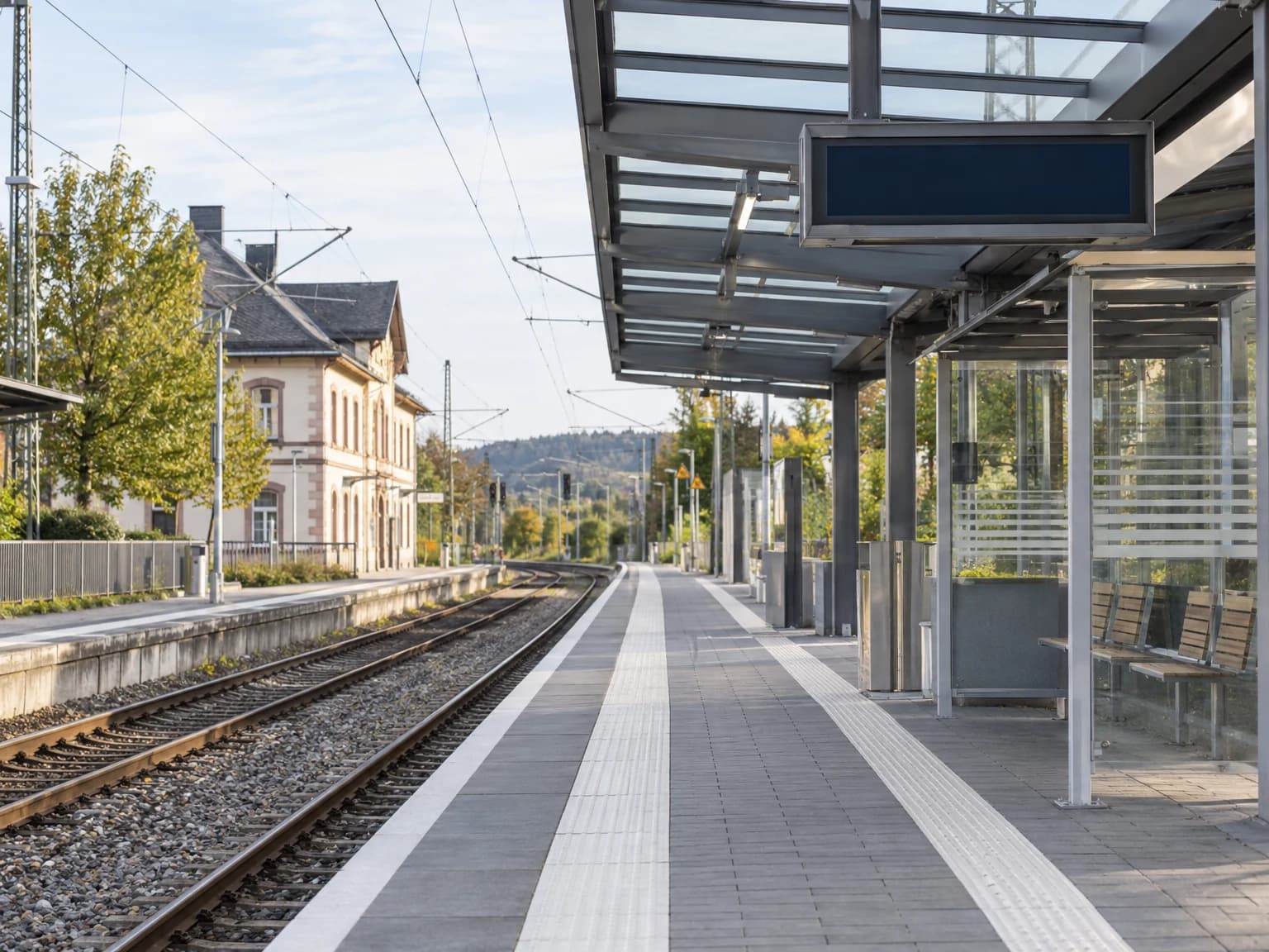 Modernisierter Bahnsteig eines Regionalbahnhofs mit Dach, Blindenleitsystem und Wartehalle