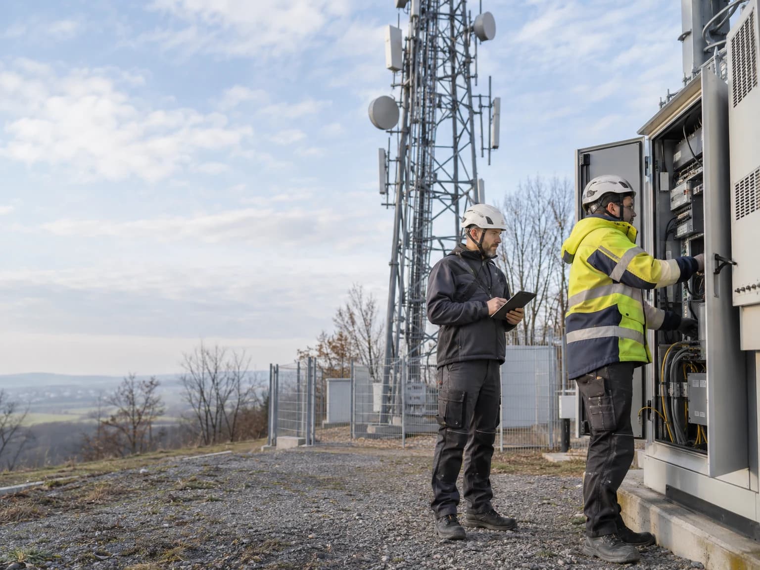 Techniker an einem Funkmast mit Antennen und Technikschrank